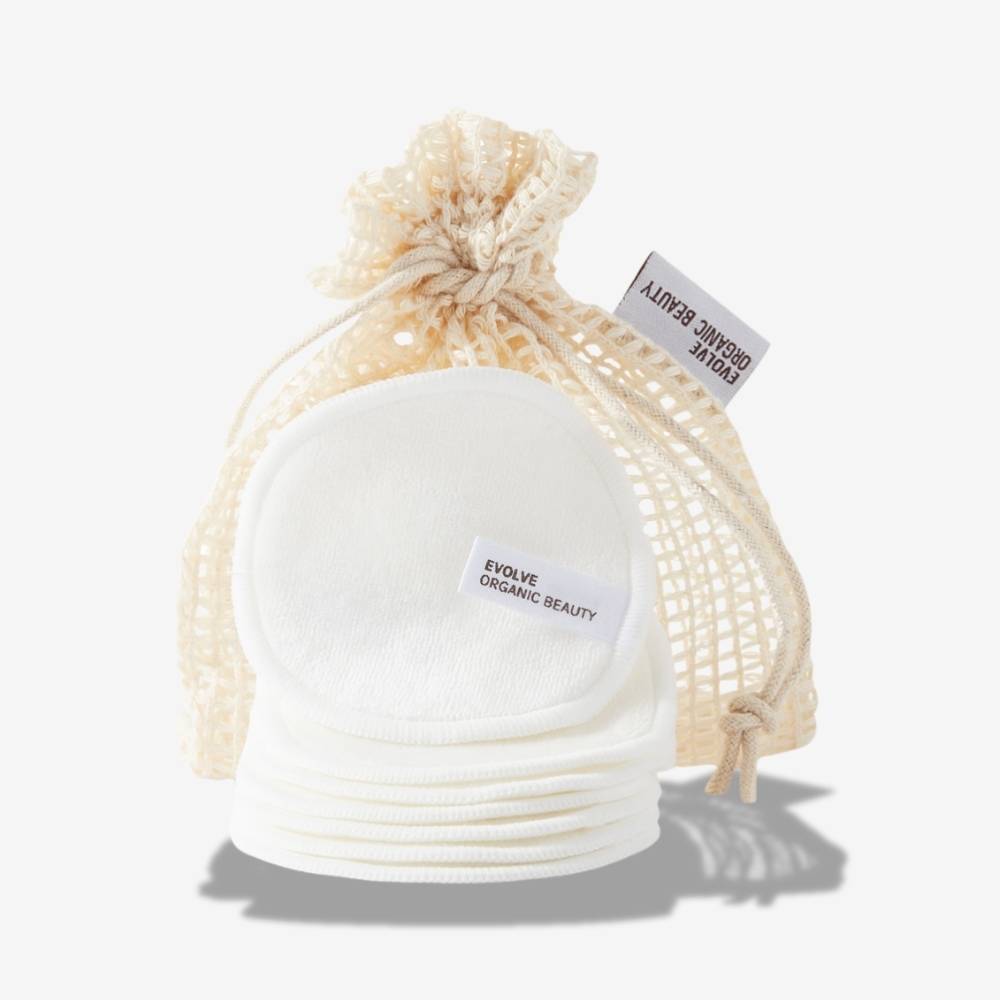 Set of 7 Evolve Organic Beauty Reusable Bamboo Makeup Pads in front of a natural mesh drawstring bag on an off-white background with a shadow underneath