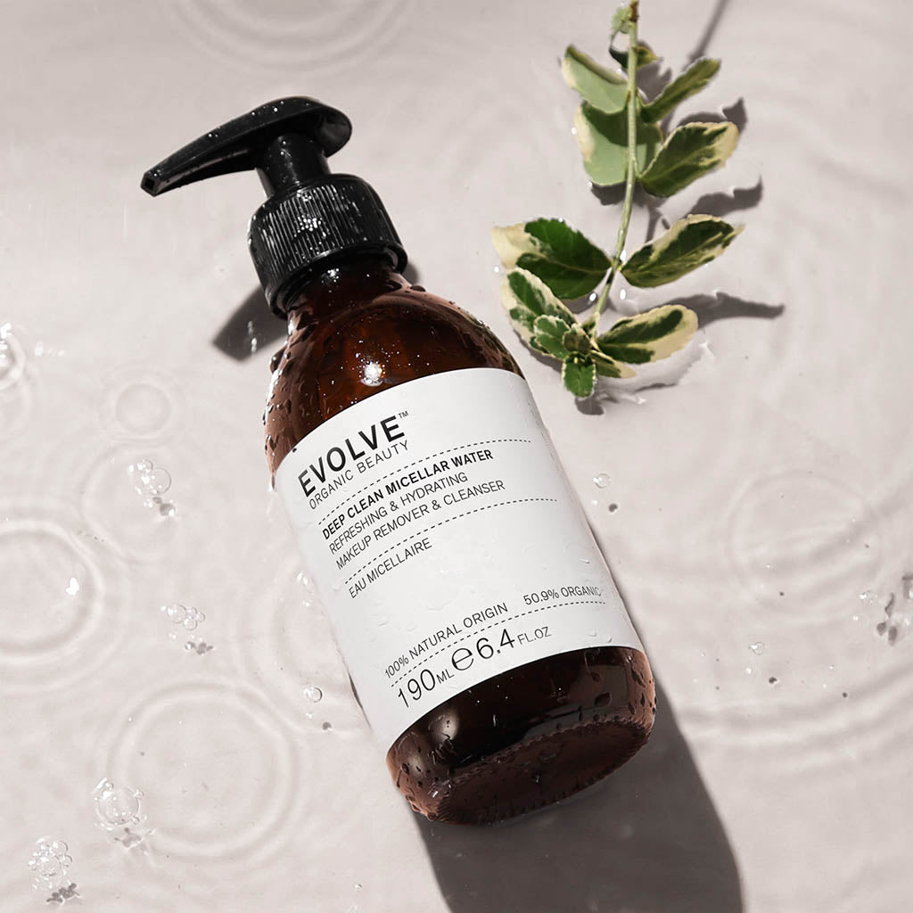 misted bottle of deep clean micellar water on top of water surrounded by water drops and leafy green plant on the side