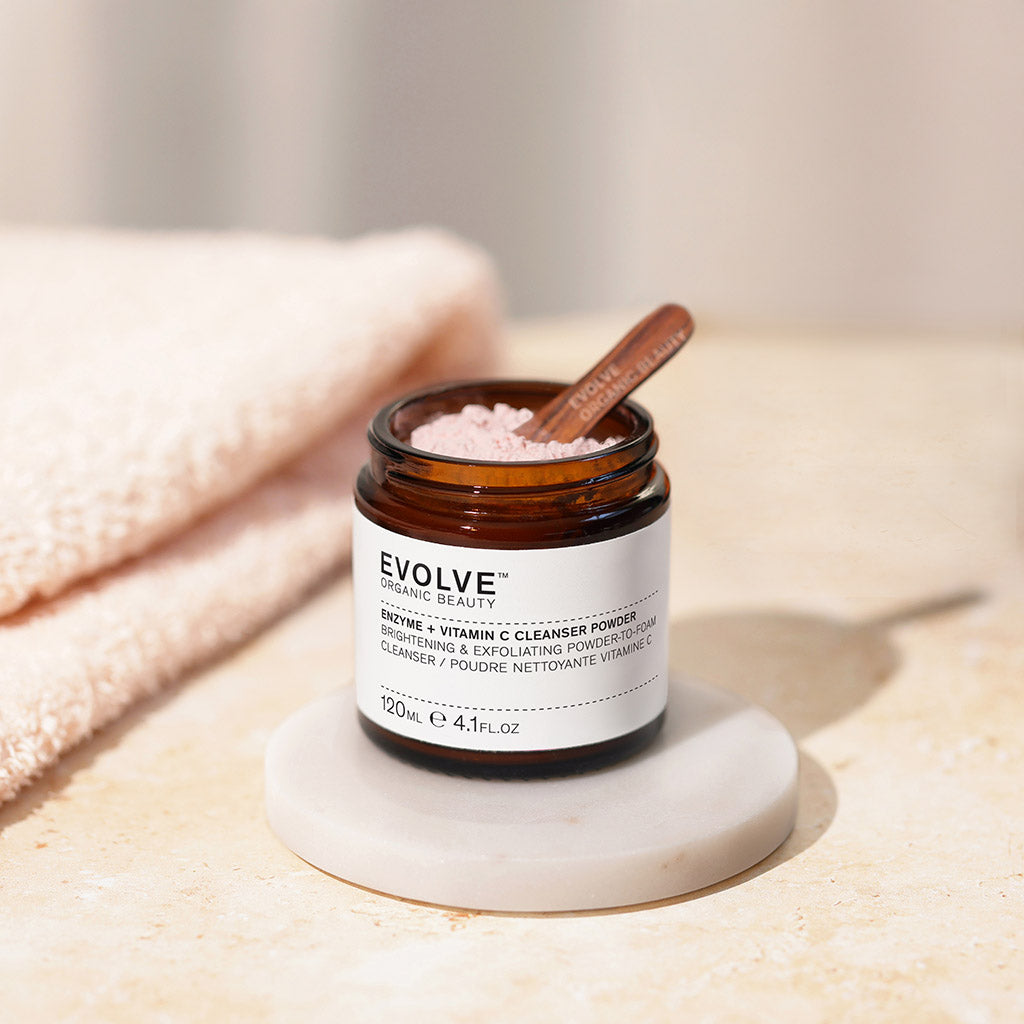 open jar of enzyme + vitamin c powder cleanser with a small wooden spatula inside on a marble coaster with a soft folded towel on the side