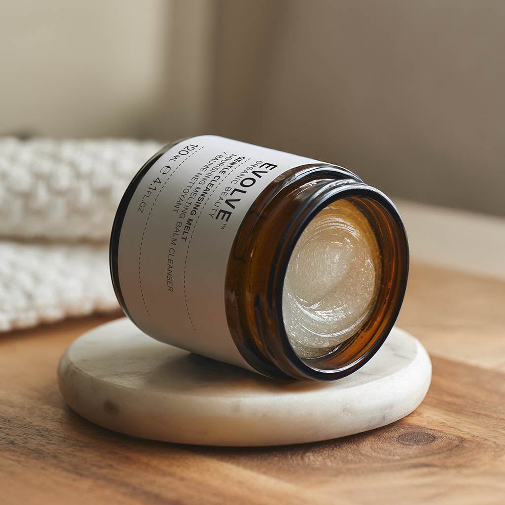 open jar of gentle cleansing melt showing its balmy texture laid sideways on top of marble coaster laid on the wooden surface with soft piece of white fabric in the background