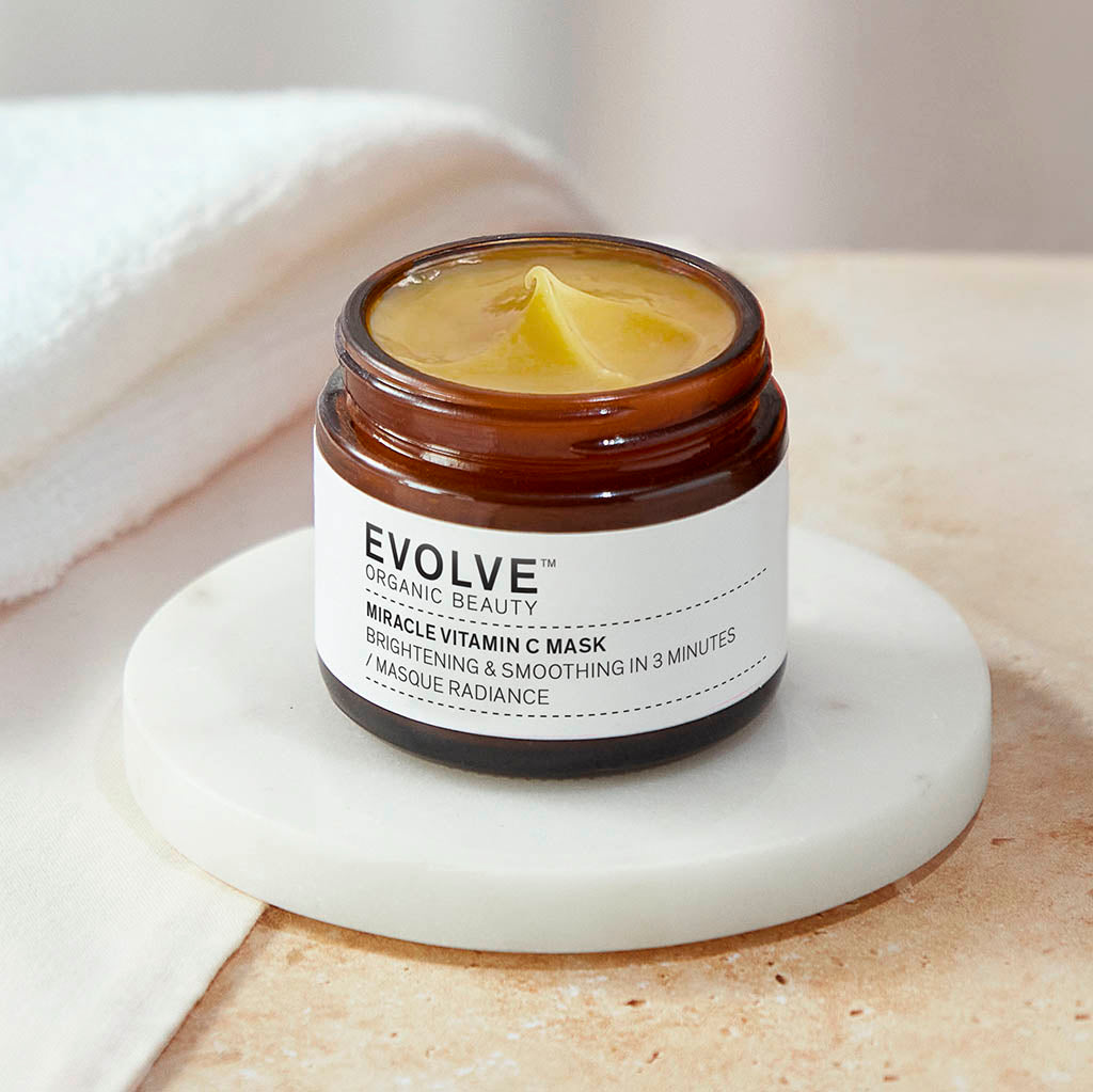 open jar of miracle vitamin c mask showing bright orange texture of product on top of marble coaster with soft white towels in background