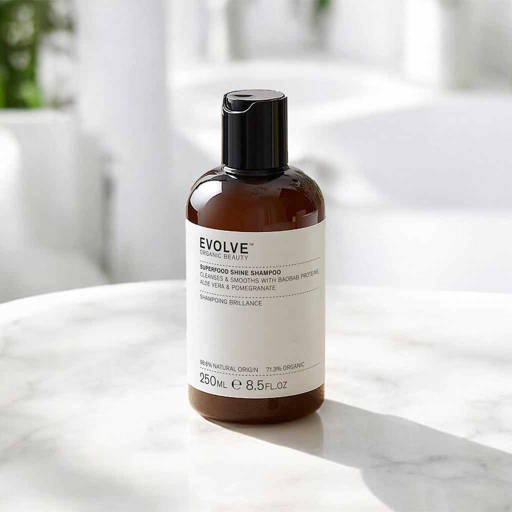 Bottle of Superfood Shine Shampoo 250ml placed on a white marble surface in dappled sunlight with soft focus background of a white room and greenery