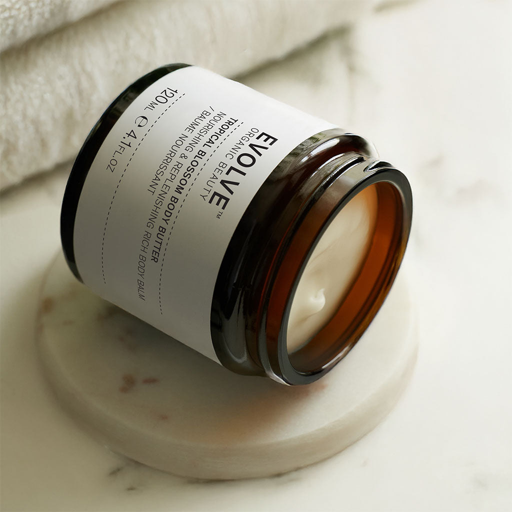 jar of tropical blossom body butter lying on its side on a marble coaster and countertop with soft towels in the background