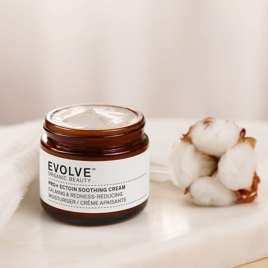 Open jar of Pro + Ectoin Soothing Cream on a marble tray next to a delicate cotton flower