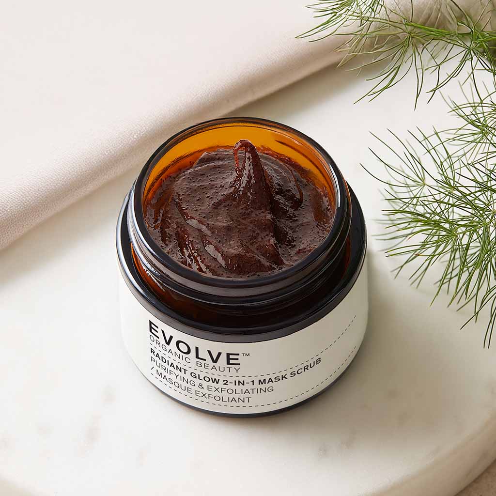 open jar of radiant glow mask showing chocolate like texture on marble tray with greenery to the right hand side
