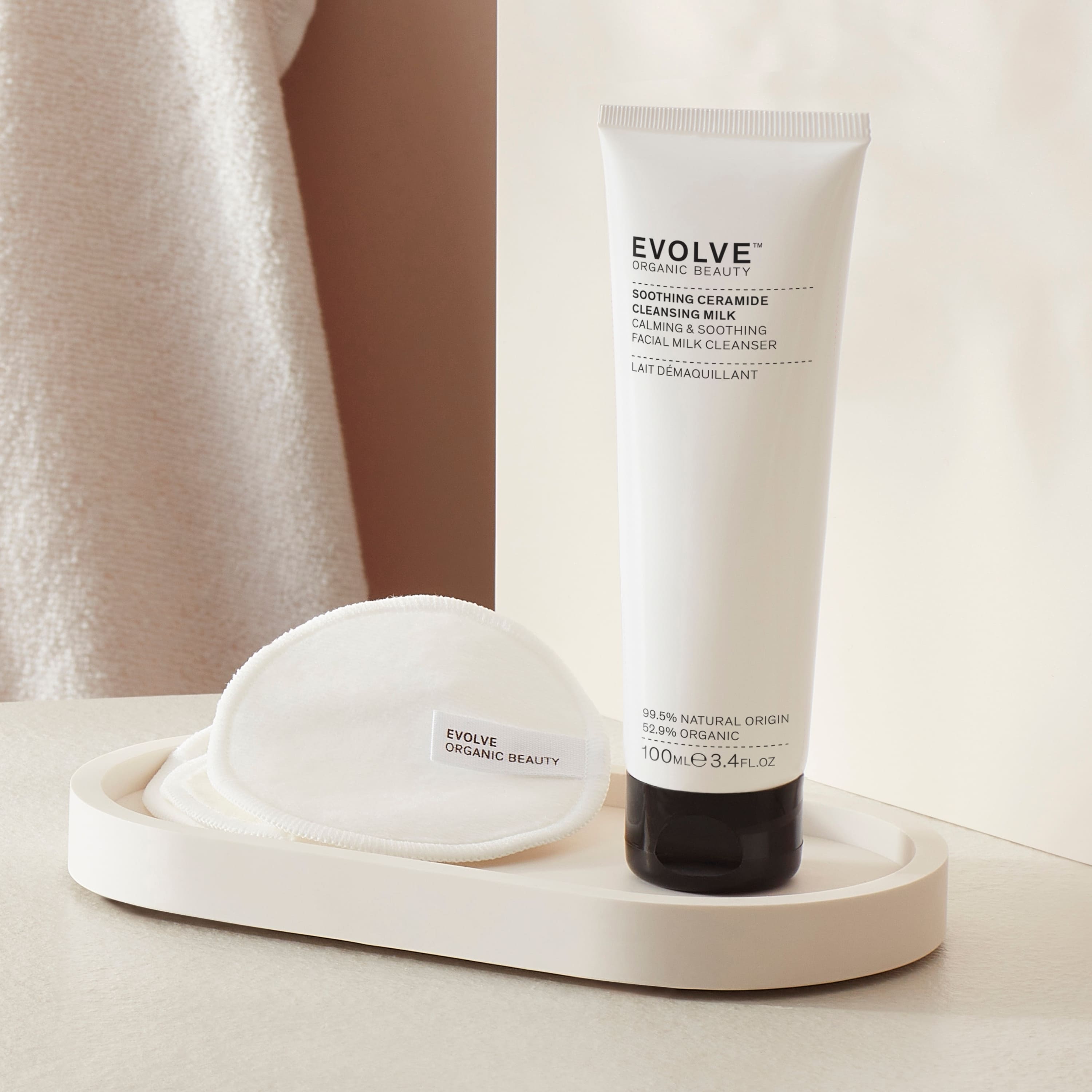 Evolve Organic Beauty soothing ceramide cleansing milk tube in a bathroom setting next to reusable bamboo pads