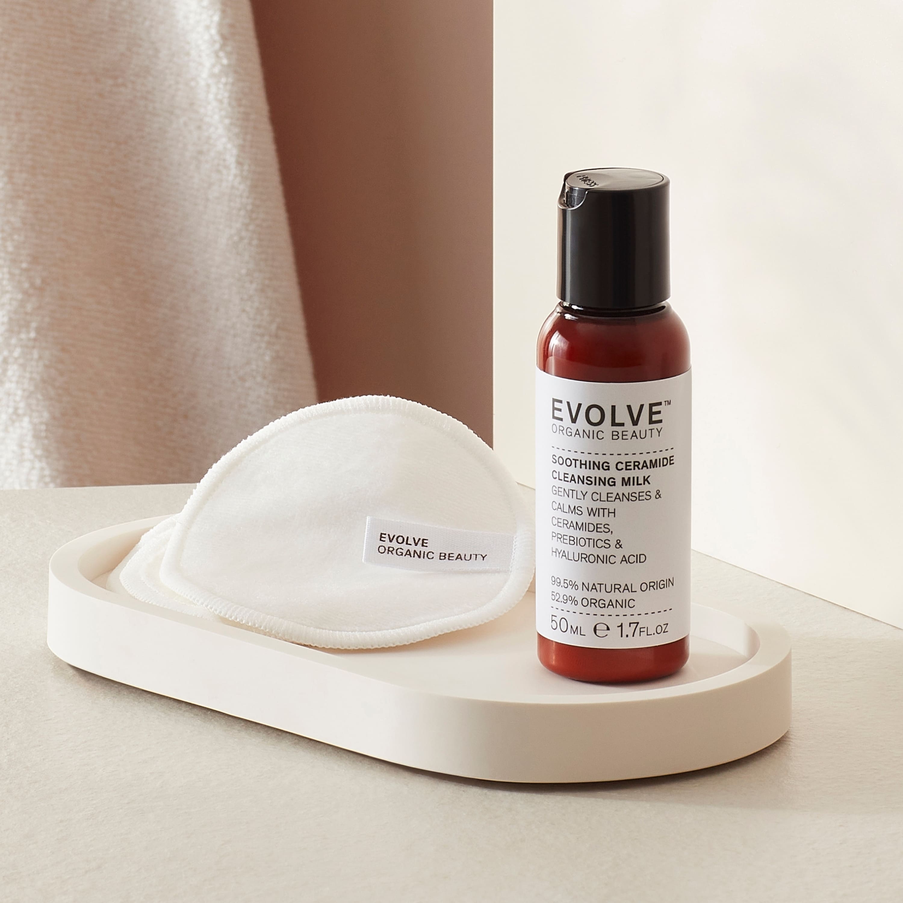 Evolve Organic Beauty soothing ceramide cleansing milk travel size bottle in a bathroom setting next to reusable bamboo pads