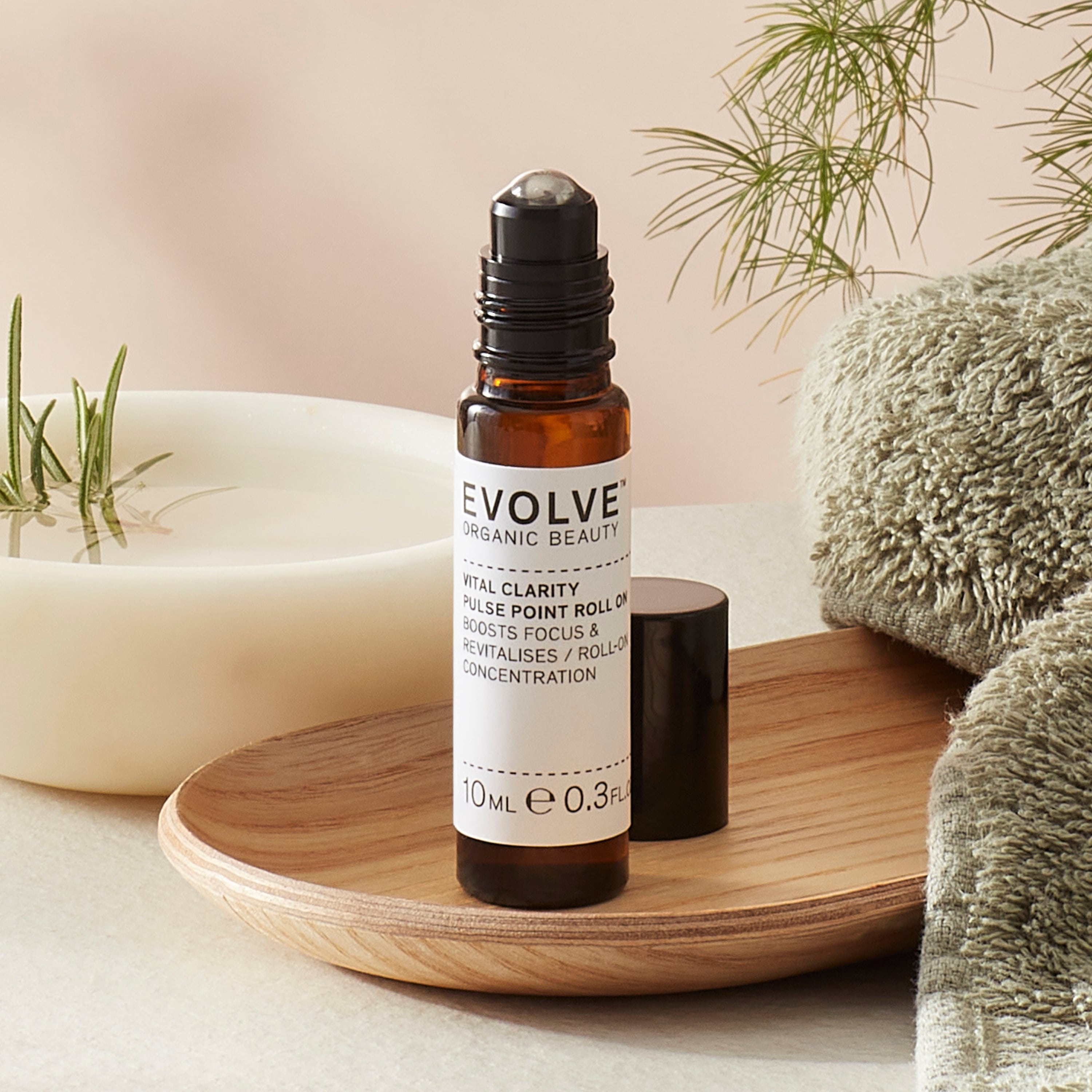 Evolve organic beauty Vital Clarity Pulse point roll on in Brown bottle with cap on a wooden tray with green towel on a beige background