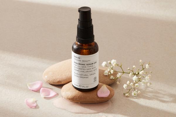 evolve organic beauty hyaluronic acid serum on pebble with flower petals around it