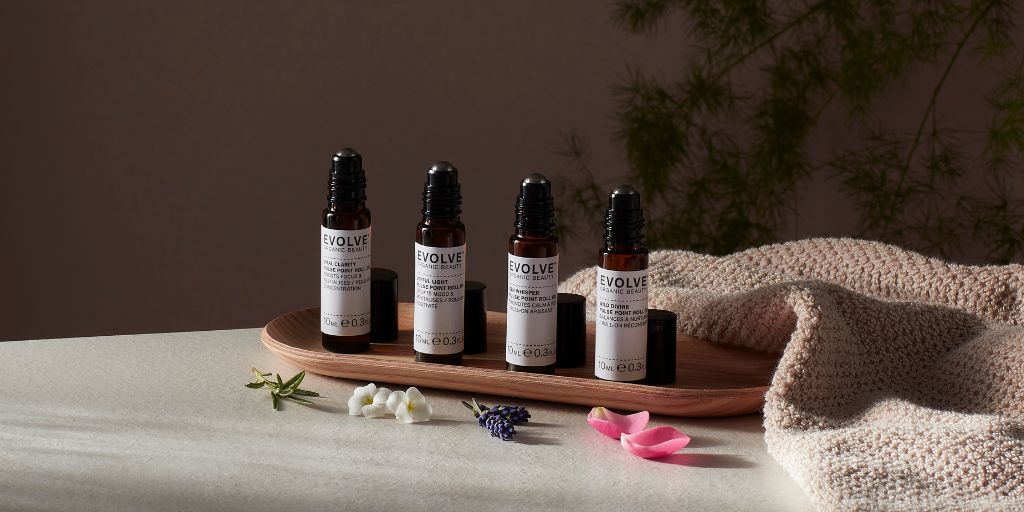 evolve new aromatherapy roller balls on shelf with dark sultry lighting and towel next to them with petals surrounding