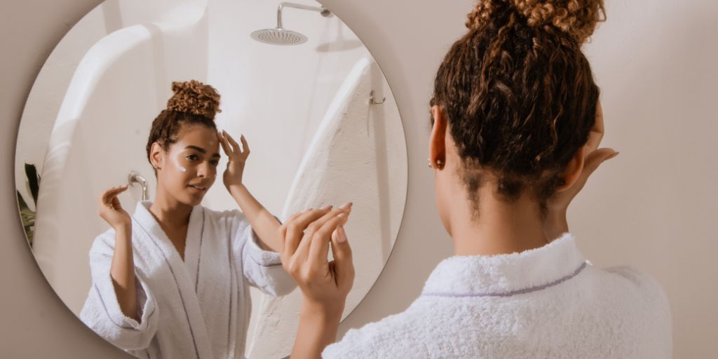 girl standing in front of bathroom mirror in bath robe doing skin care
