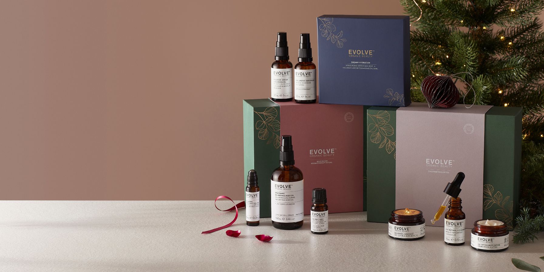 image of evolve beauty christmas sets infront of christmas tree with ribbon and products surrounding them