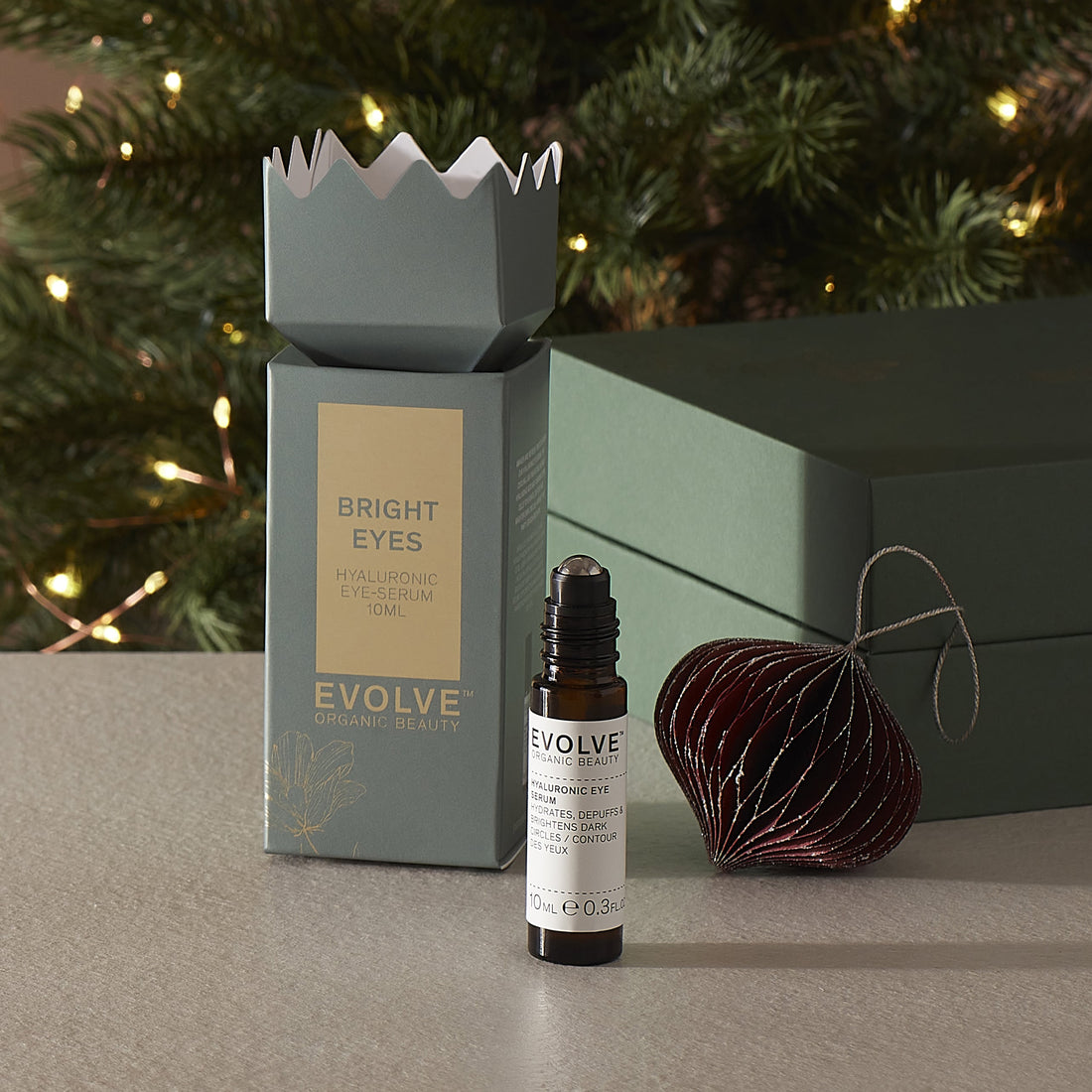 Evolve skincare hyaluronic eye serum with christmas packaging and decorative ornament on a surface with a Christmas tree in the background