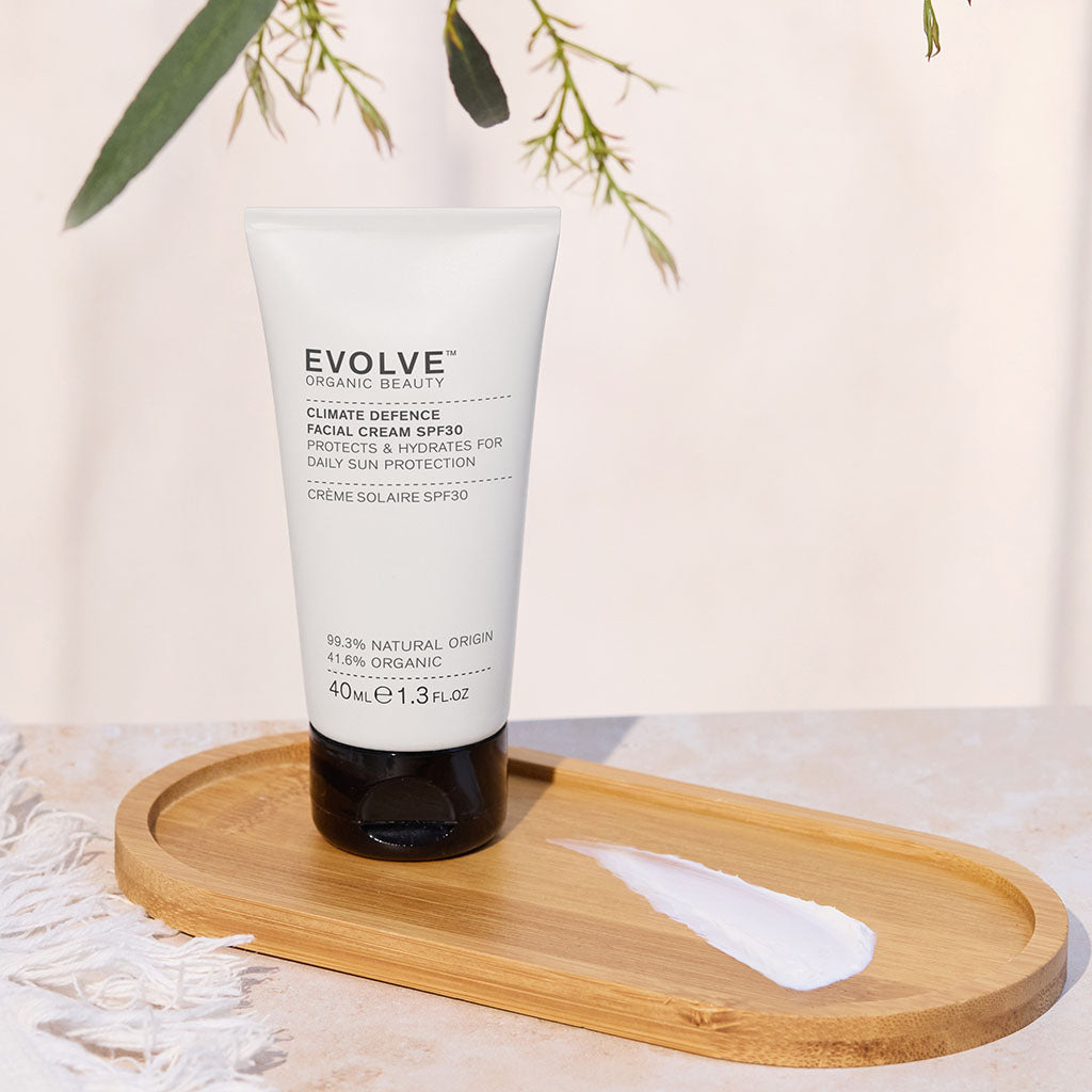 Beige tube of Climate Defence SPF30 standing on a wooden tray, beside a swatch of the cream.  A sprig of greenery hangs above it