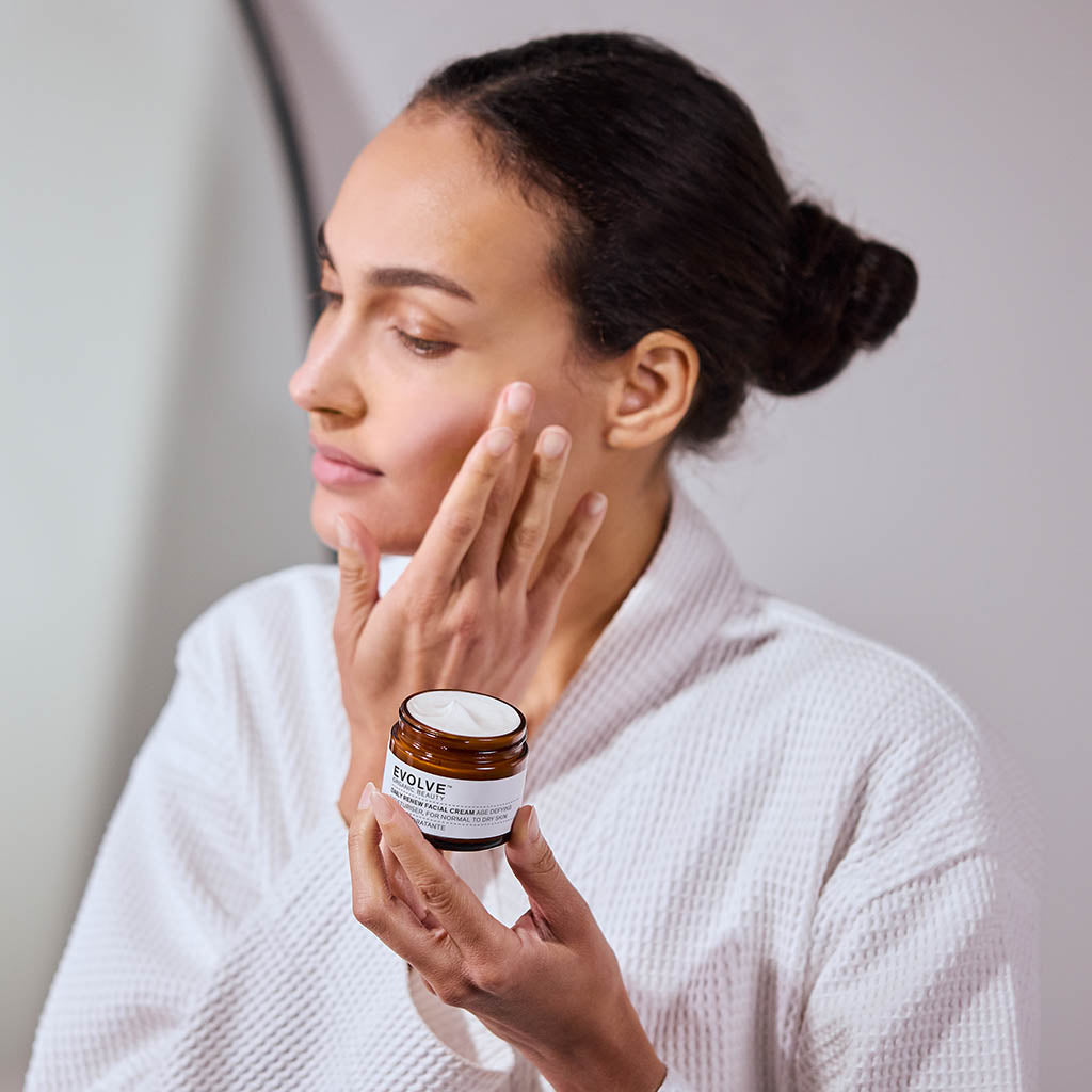 Model holding a jar of Daily Renew Facial Cream and applying it to her cheek