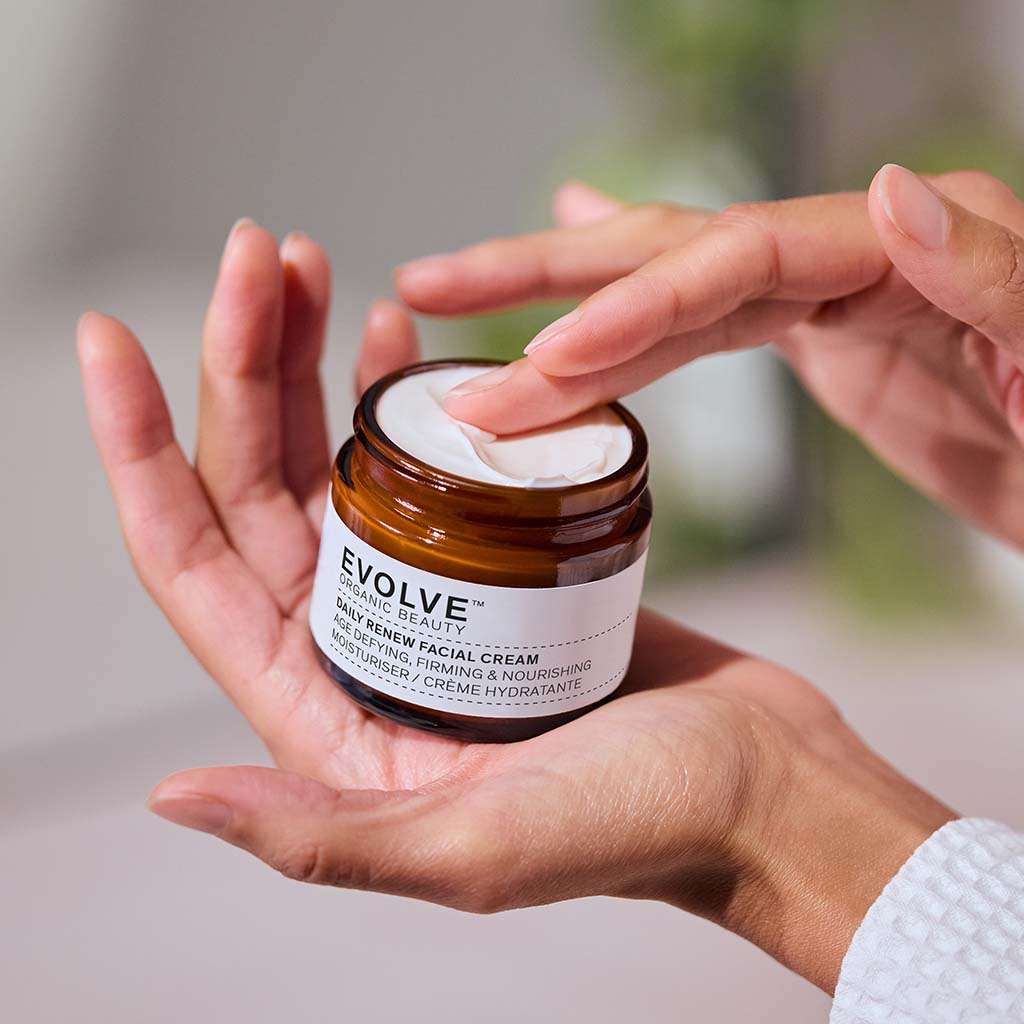 Close up of model holding a jar of Daily Renew Facial Cream, dipping her finger into the cream