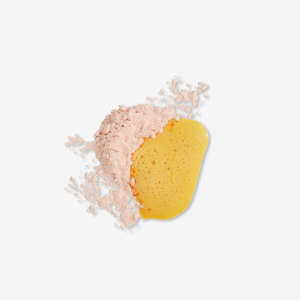 Swatch of pale orange powder turning into bright orange foam showing texture of enzyme + vitamin c powder cleanser