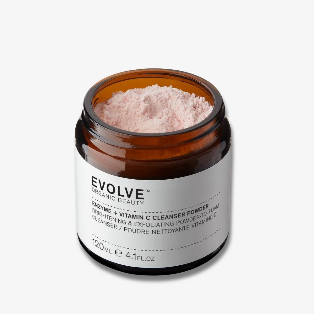Evolve Organic Beauty Enzyme + Vitamin C Powder Cleanser in brown open jar filled with pale orange powder on off white background with shadow behind