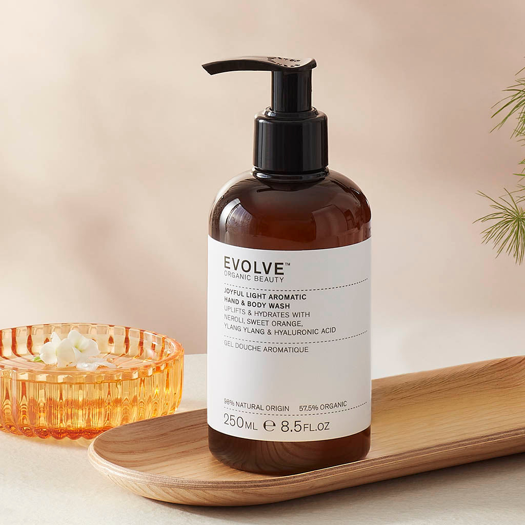Evolve organic beaity Joyful Light Aromatic Wash in Brown bottle with pump dispenser  on a wooden tray with a beige background
