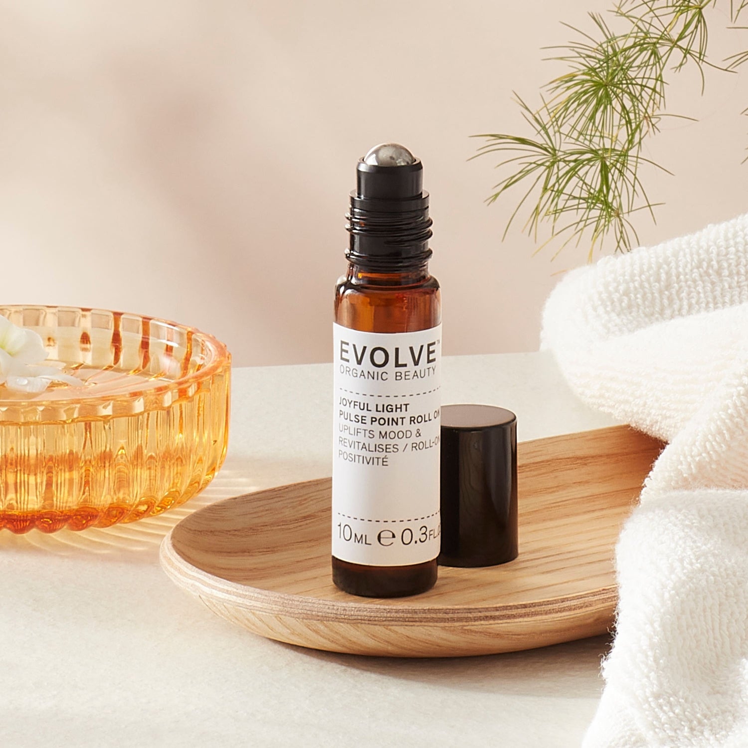 Evolve organic beauty Joyful Light Pulse Piont Roll On in Brown bottle with cap on a wooden tray with towel on a beige background