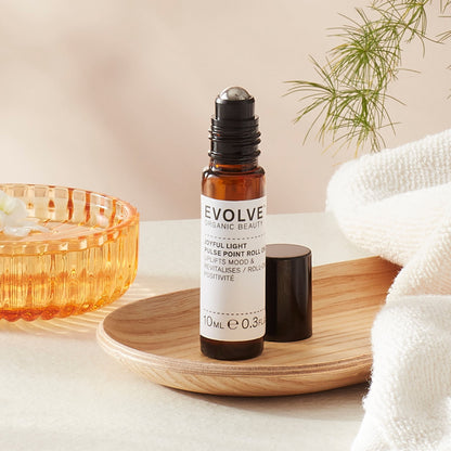 Evolve organic beauty Joyful Light Pulse Piont Roll On in Brown bottle with cap on a wooden tray with towel on a beige background