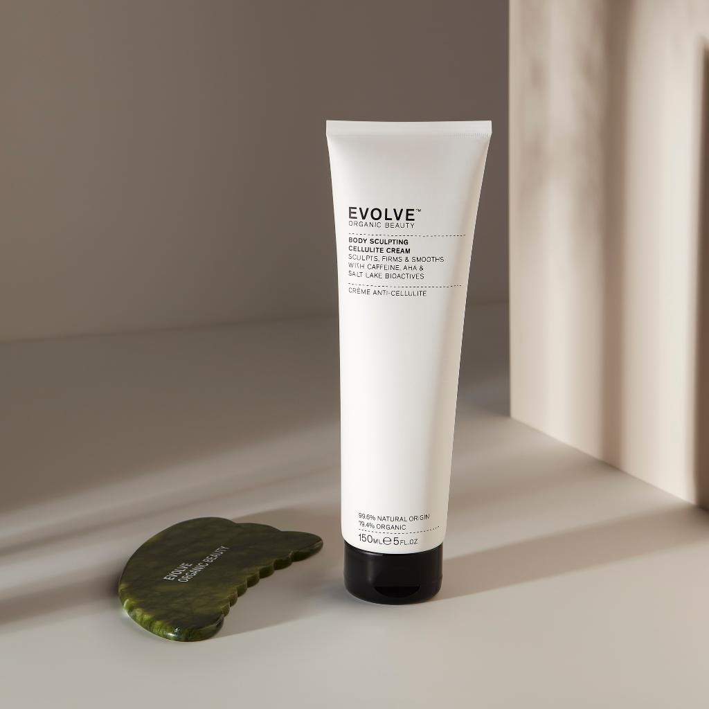 body sculpting cellulite cream and jade body gua sha on light beige background with shadows