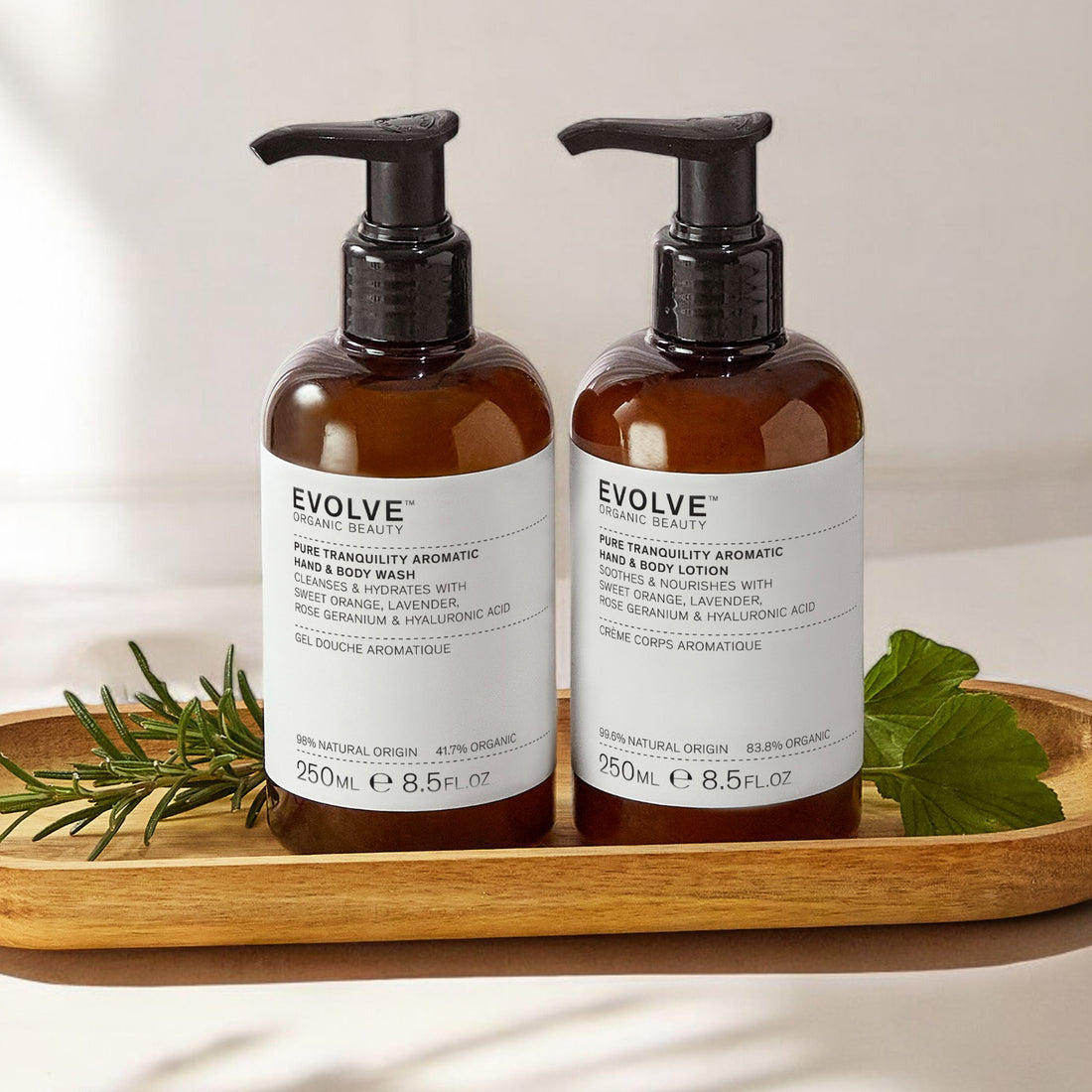 bottle of pure tranquility aromatic wash and  lotion on wooden tray with rosemary and geranium leaves on beige background