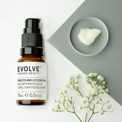bottle of Eye and Lip Contour in a contemporary shot, with a sprig of white flower and glass dish with a pump of cream