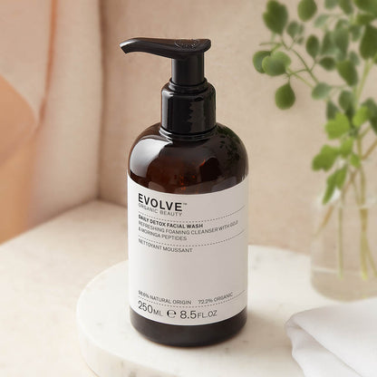 bottle of evolve daily detox facial wash placed on a black marble with a vase and green leafy plant on the side