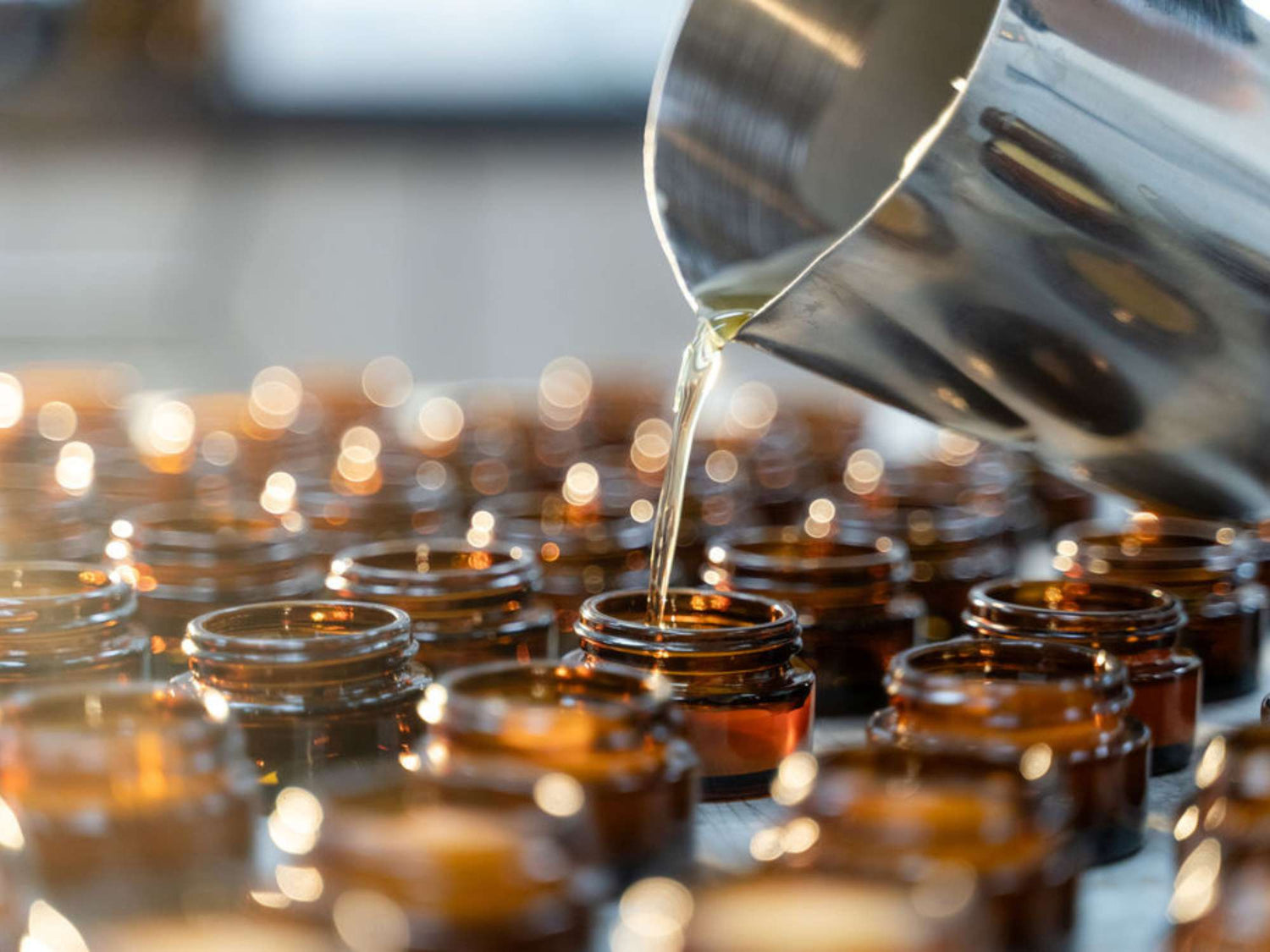 liquid pouring from large metal jug into amber glass jars with light shining through them