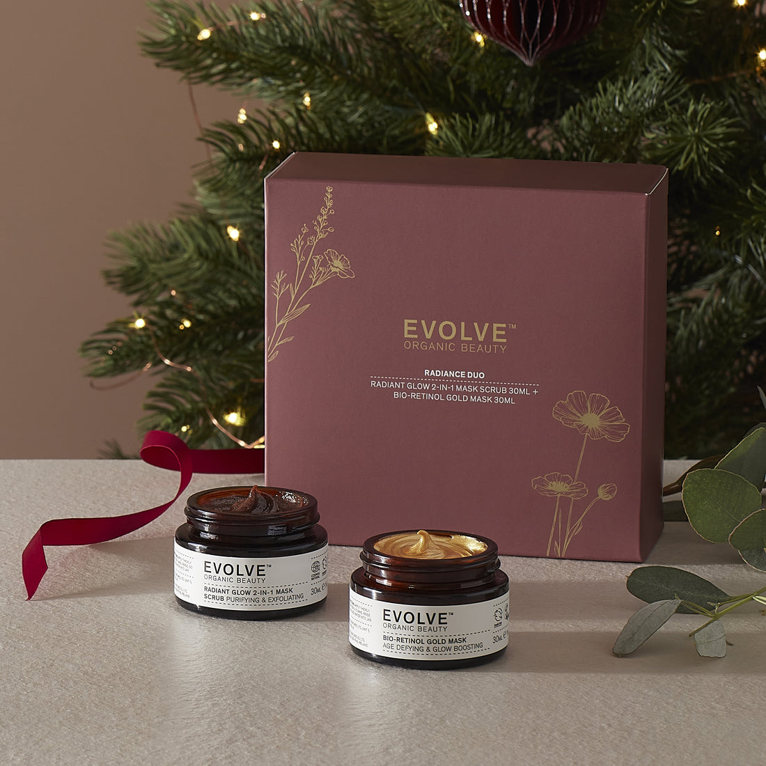 Evolve Organic Beauty radiance duo including radiant glow 2-in-1 mask and bio-retinol gold mask with packaging in front of a Christmas tree.