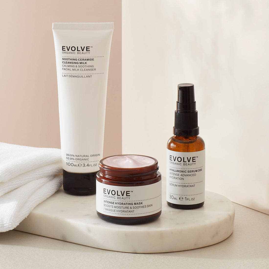 sensitive skin Saviours set bundle including soothing ceramide cleansing milk in sugarcane tube,hyaluronic serum 200 in broung glass bottle with pump  and intense hydrating maskin brown glass jar with black lid in soft beige setting with towel and products on a marble coaster