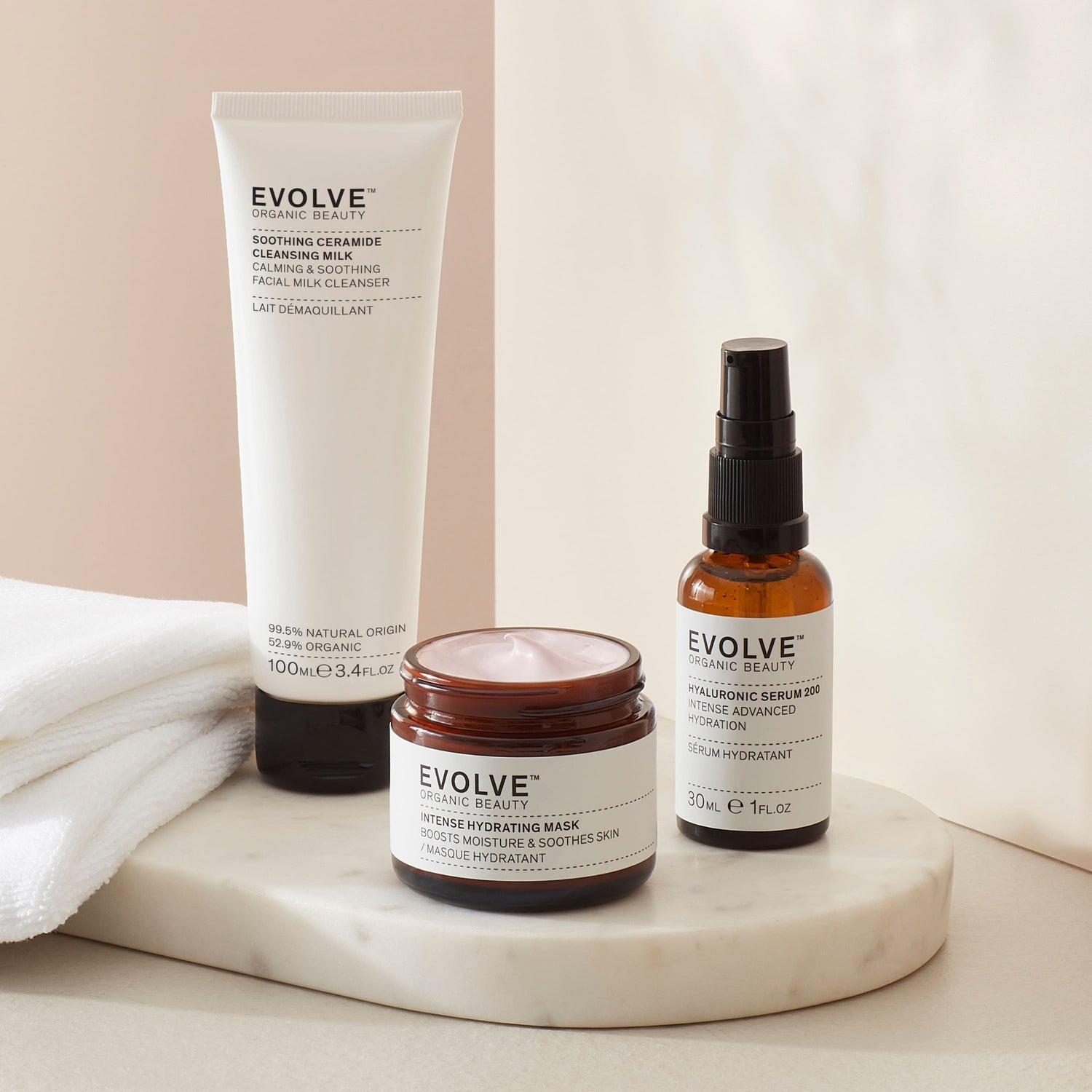 sensitive skin Saviours set bundle including soothing ceramide cleansing milk in sugarcane tube,hyaluronic serum 200 in broung glass bottle with pump  and intense hydrating maskin brown glass jar with black lid in soft beige setting with towel and products on a marble coaster