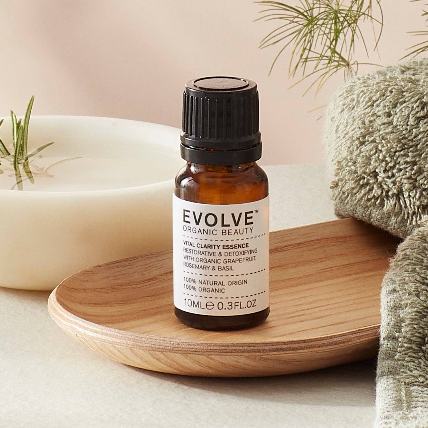 Evolve organic beauty Vital Clarity Essence in Brown bottle with cap on a wooden tray with green towel on a beige background