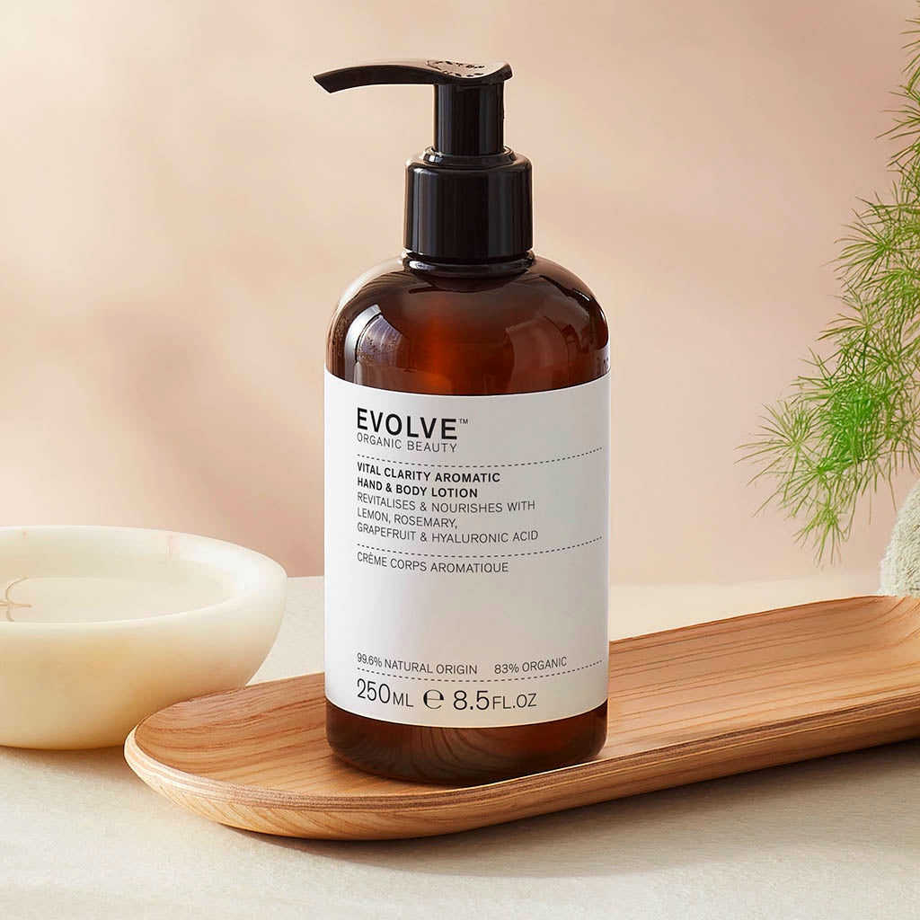 Evolve organic beauty Vital Clarity aromatic lotion in Brown bottle with cap on a wooden tray with green towel on a beige background