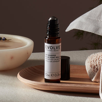 Evolve organic beauty Zen Whisper Pulse Point Roll On in Brown bottle with cap on a wooden tray with beige towel  on a dark beige background
