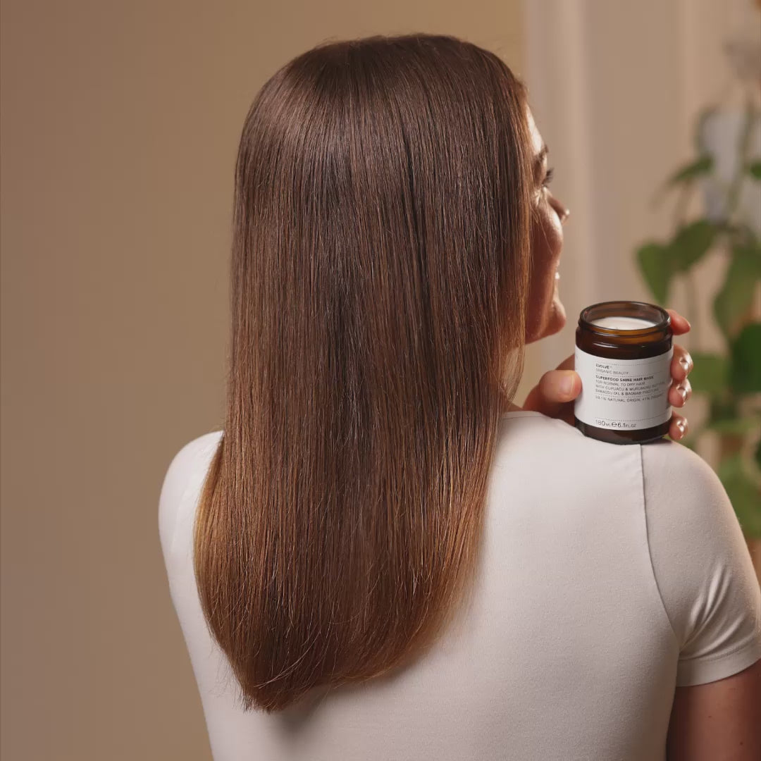 Video of a woman holding a jar of Superfood Shine Hair Mask then scooping out a handful of the mask to show the texture, followed by her shaking her frizzy hair and then showing off smooth silky hair.